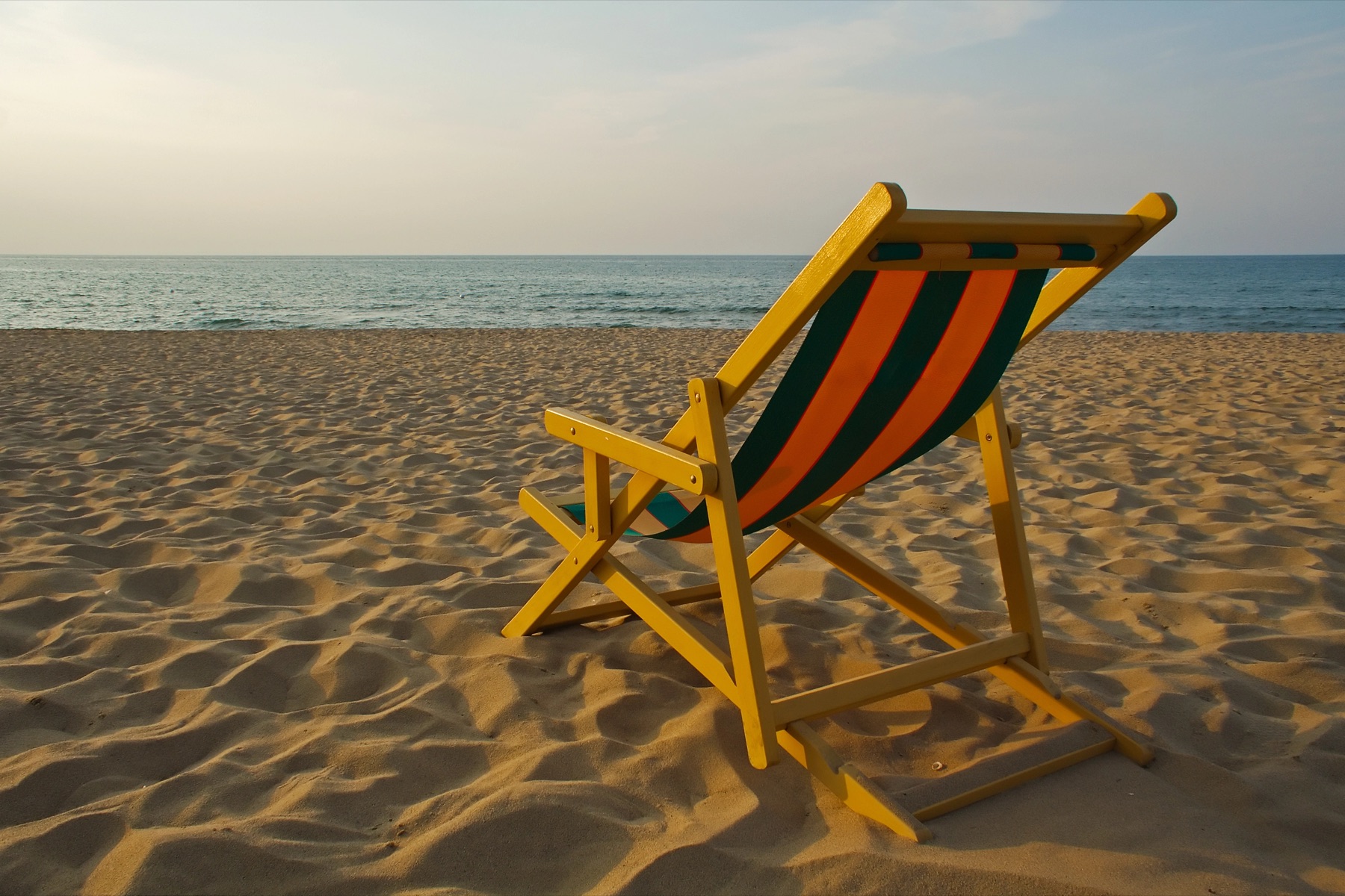 An empty chair on a beach, facing the sea